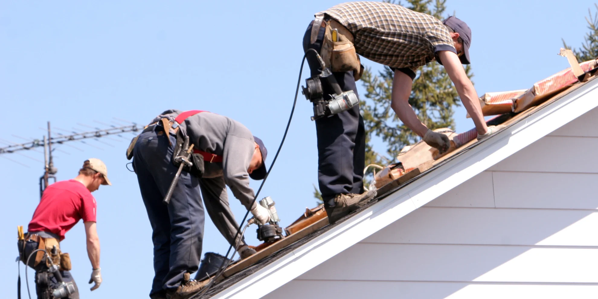 three people simultaneously installing roof shingles